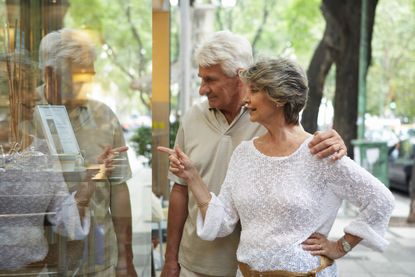 Senior couple looking in shop window, woman pointing