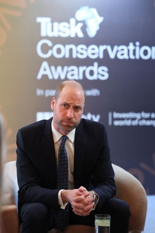 Prince William wearing a suit sitting in a chair with his hands clasped