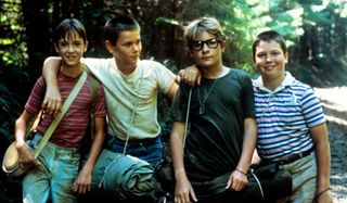Wil Wheaton, River Phoenix, Corey Feldman, and Jerry O'Connell stand together in the woods in Stand By Me.