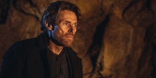 Willem Dafoe in a cave, dressed in all black