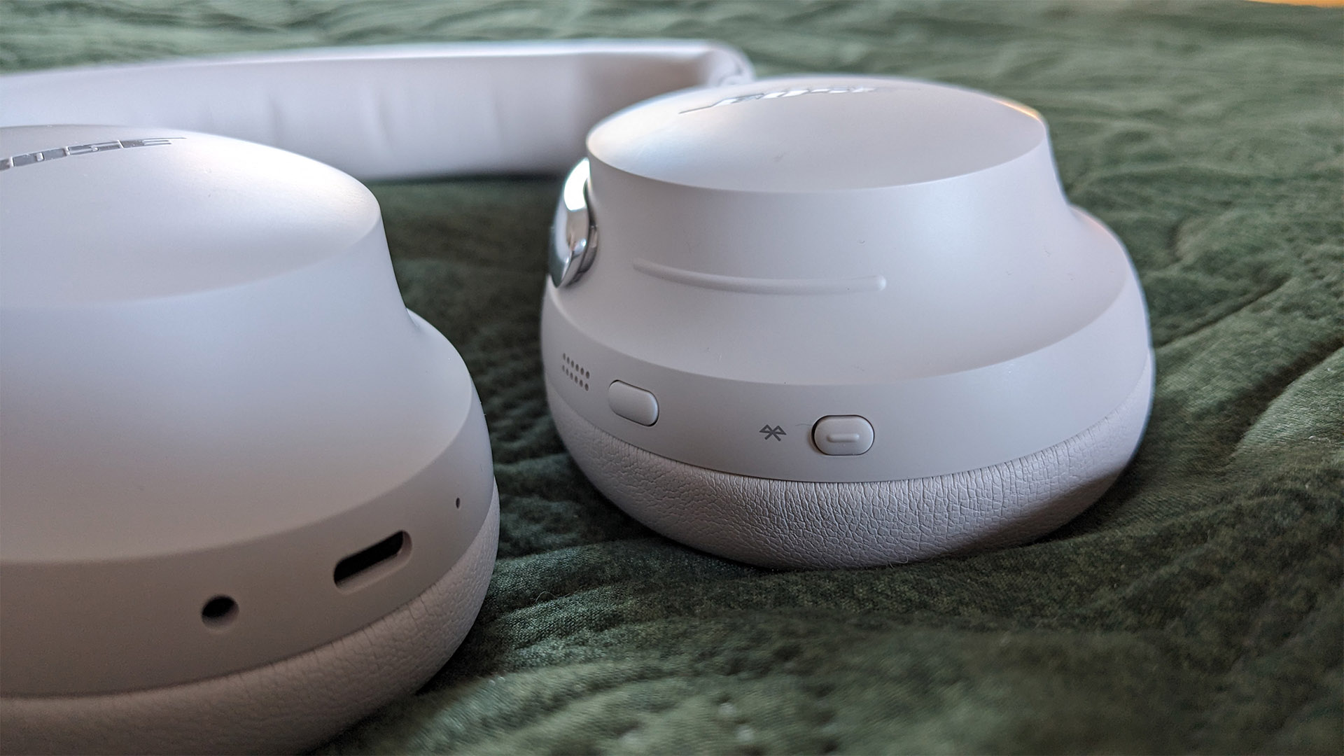 Bose QuietComfort Ultra Headphones (2nd Gen) noise-cancelling headphones on green fabric detail of on-earcup controls
