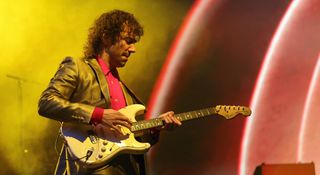 Albert Hammond Jr. of the Strokes wears a red shirt and a grey suit jacket as he plays his Fender Stratocaster onstage with the Strokes.