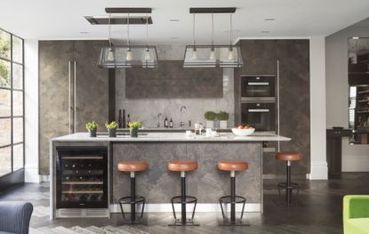 A modern grey kitchen island with orange bar stools and pendant lighting