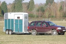 A 4x4 towing a two-horse trailer across a field