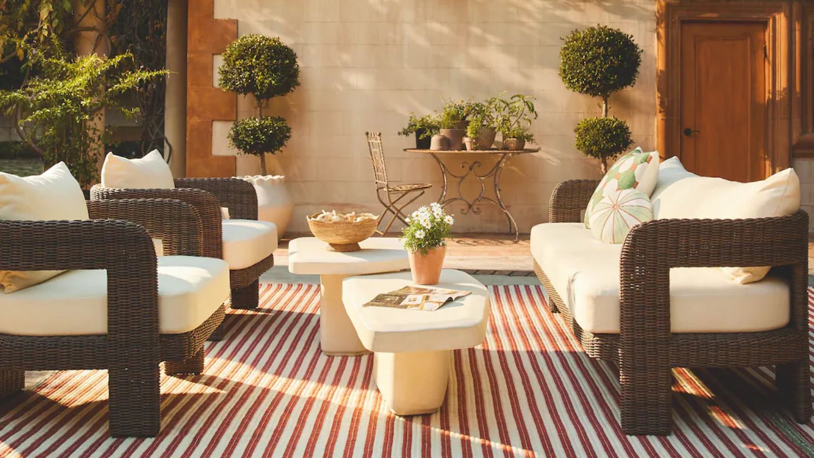 italian villa european-style outdoor garden with a patio set made from dark brown rattan sat on a red and white striped rug with bay trees and ornate antique furniture accents