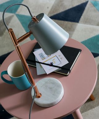 marble and copper task lamp on round shaped pink colour table with blue coffee mug