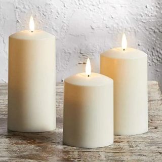 Three cream coloured flameless candles on a wooden table.