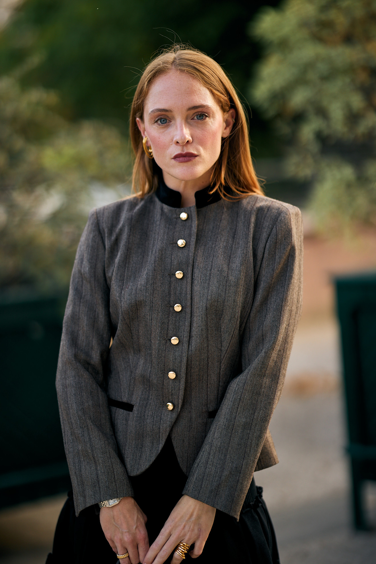 a white woman with red hair in a gray jacket with gold buttons wearing dark red lipstick