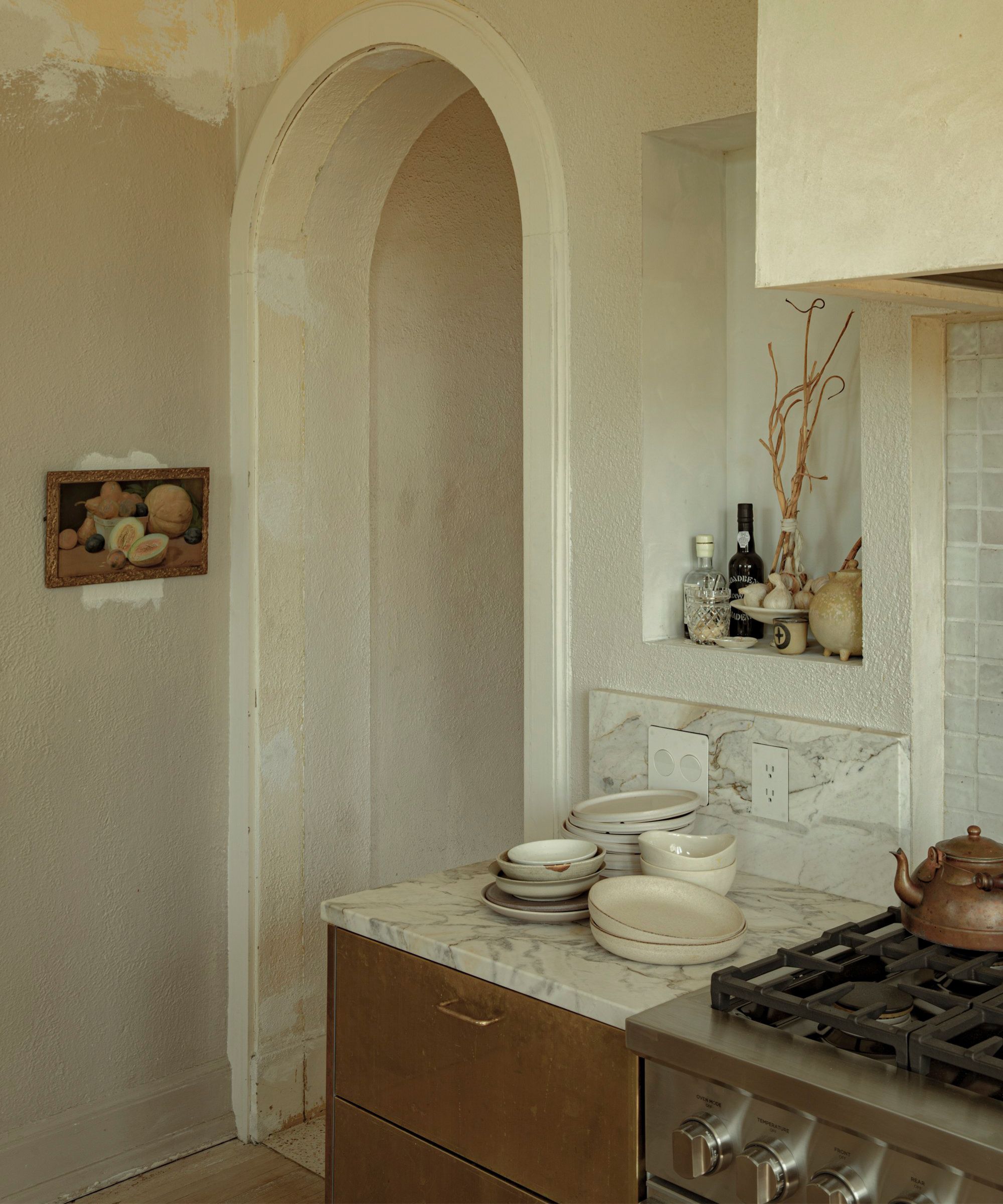 a rustic plaster finished historic kitchen remodeled with brass cabinetry, a plaster cook hood, marble counters and storage niches