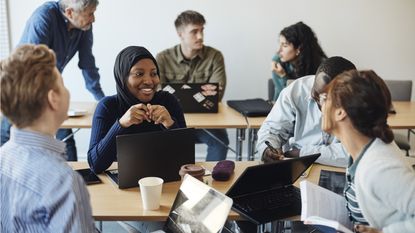 A group of college students chat in a classroom.