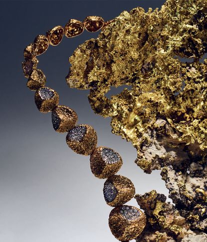 A close-up of seven connected gold / diamond stones adjacent to a large gold-coloured leaf object. 