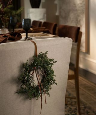 A Christmas wreath hung on the back of a dining chair