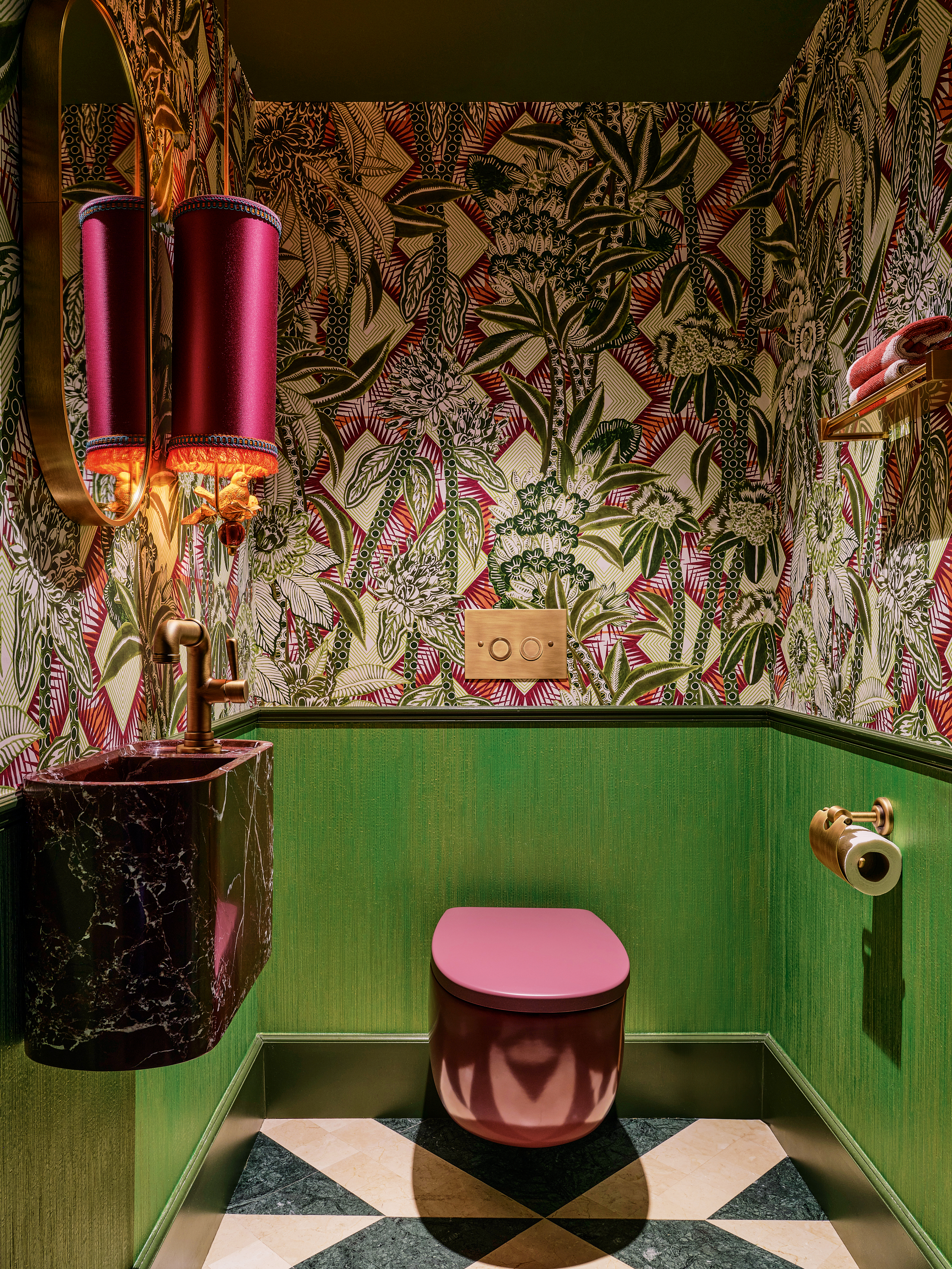 Powder room with green paneling, green and pink patterned wallpaper, pink sanitaryware and pink satin wall light