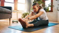Woman doing lower back stretches on yoga mat in living room wearing activewear