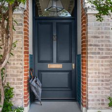 small front door porch, dark grey front door with turquoise tiles halfway up in the porch, umbrella lent up, lantern pendant