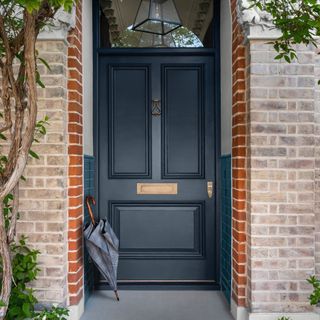 small front door porch, dark grey front door with turquoise tiles halfway up in the porch, umbrella lent up, lantern pendant