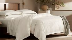 White sheets, pillows and comforter on a bed with a gray-green throw against cream walls.