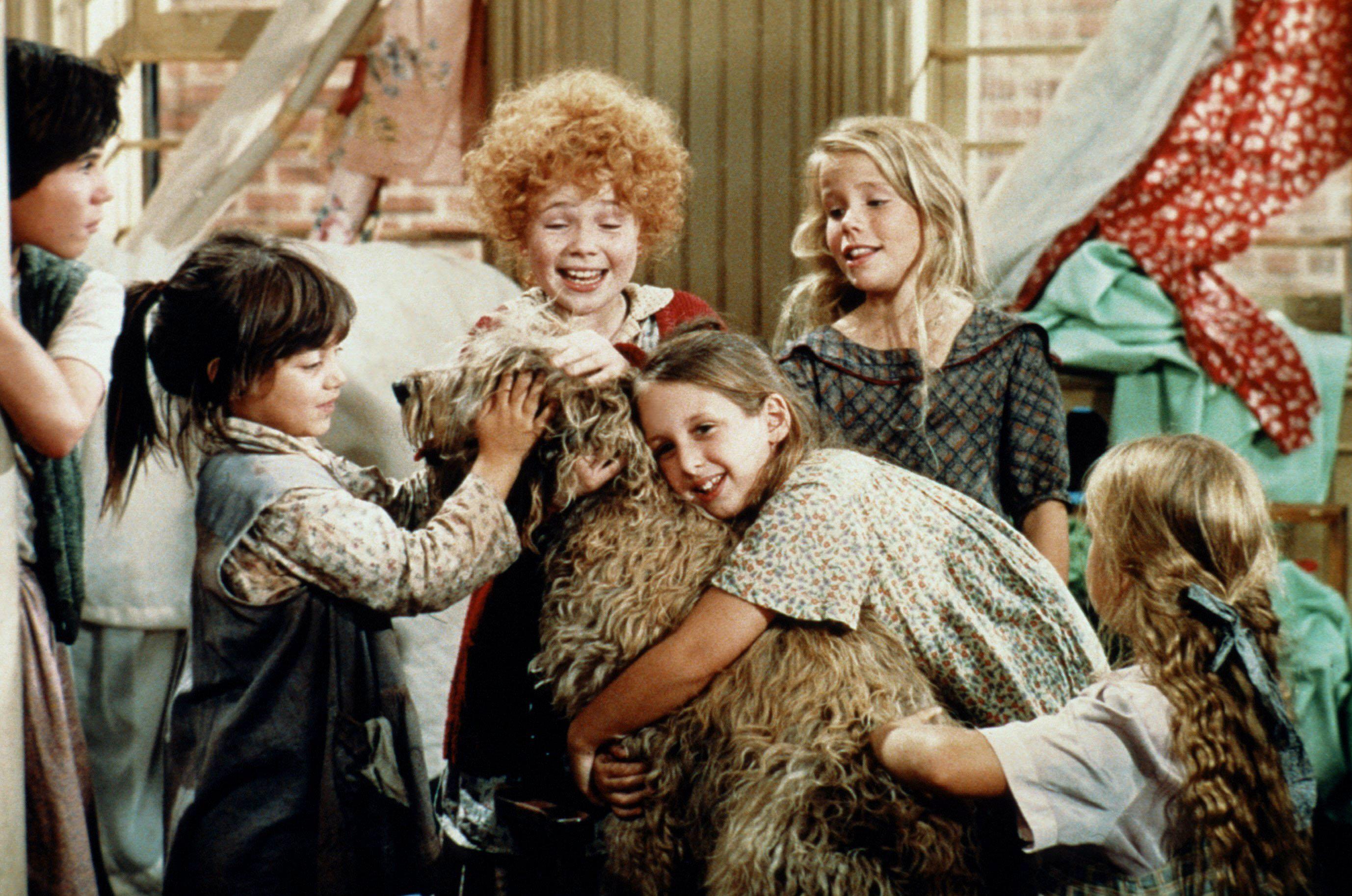 Scene from the film Annie (1982), showing a group of children gathered around and hugging Sandy the dog, an otterhound, inside the orphanage
