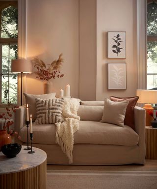 A living room with a beige couch with pillows and a throw on it, a beige wall behind it with two windows either side, and a coffee table in front