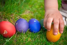A child's hand reaches out to grab an Easter egg