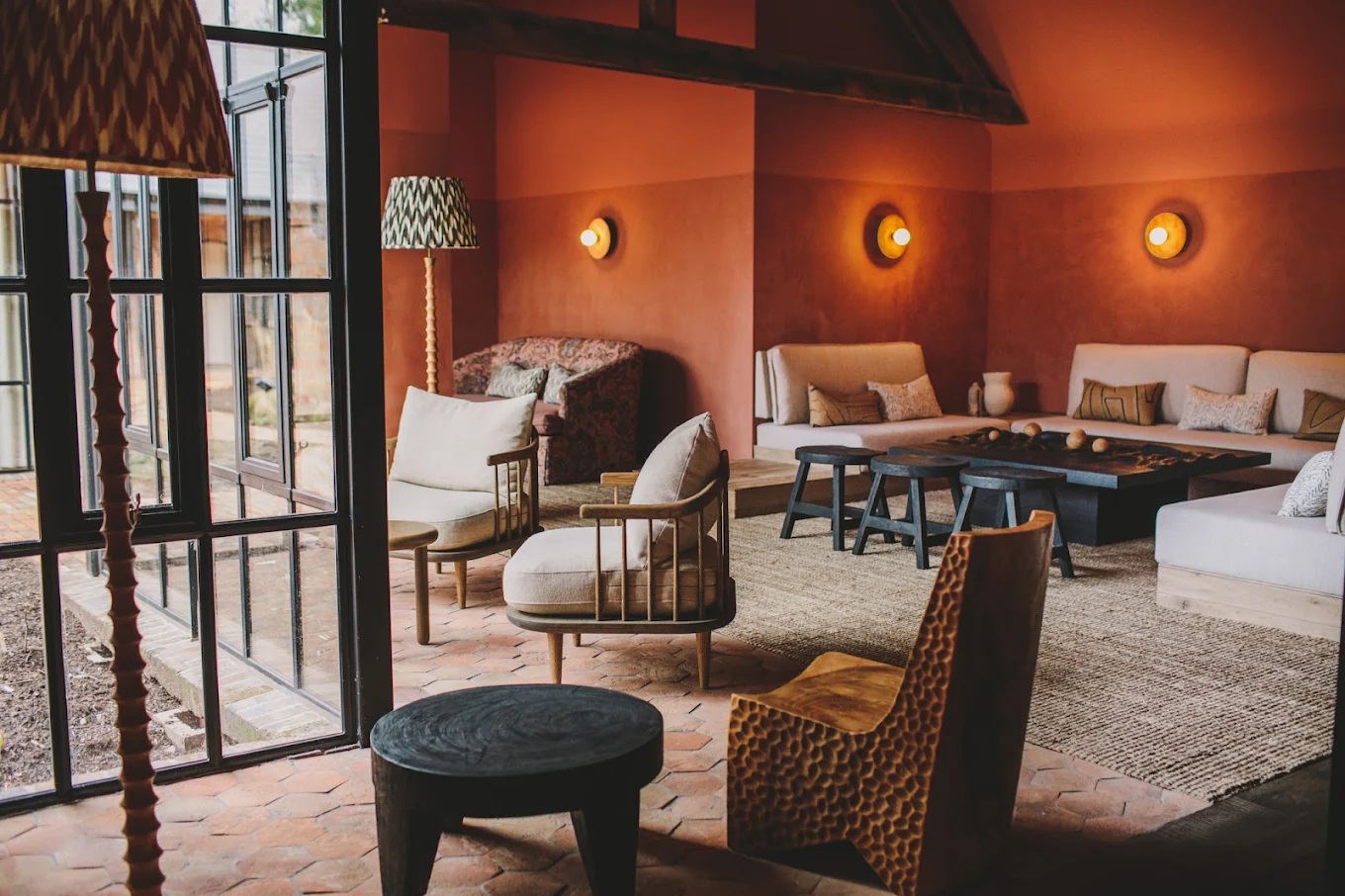 A quirky-cool hotel lounge is filled with sculptural rattan, wood, and textile textural designs, warm Art Deco spherical lighting, and brought to life by the orange paint that covers its warm walls.