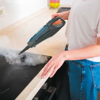 Closeup of a woman cleaning a hob with a handheld Hoover steam cleaner.