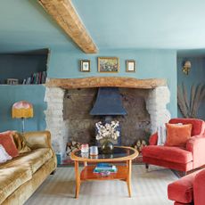 blue colour drenched living room with red velvet armchair and yellow velvet sofa and wood burner in inglenook fireplace 