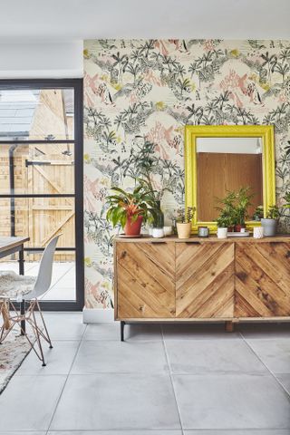 Corner of kitchen with patterned wallpaper, wooden sideboard and large format grey floor tiles