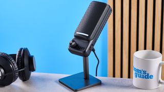 the NZXT capsule elite gaming mic, a condenser cardioid microphone in black photographed against a blue background. there are two control dials on the mic body and two RGB LED panels