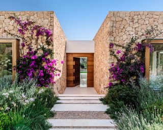 The front entrance of an Ibizan villa with local stone walls and a contemporary door in Iroko wood