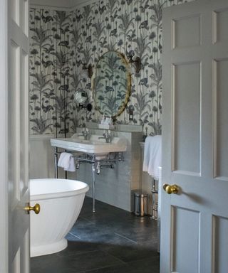 Bathroom with wallpaper with white background, freestanding bath tub, black tiles on floor