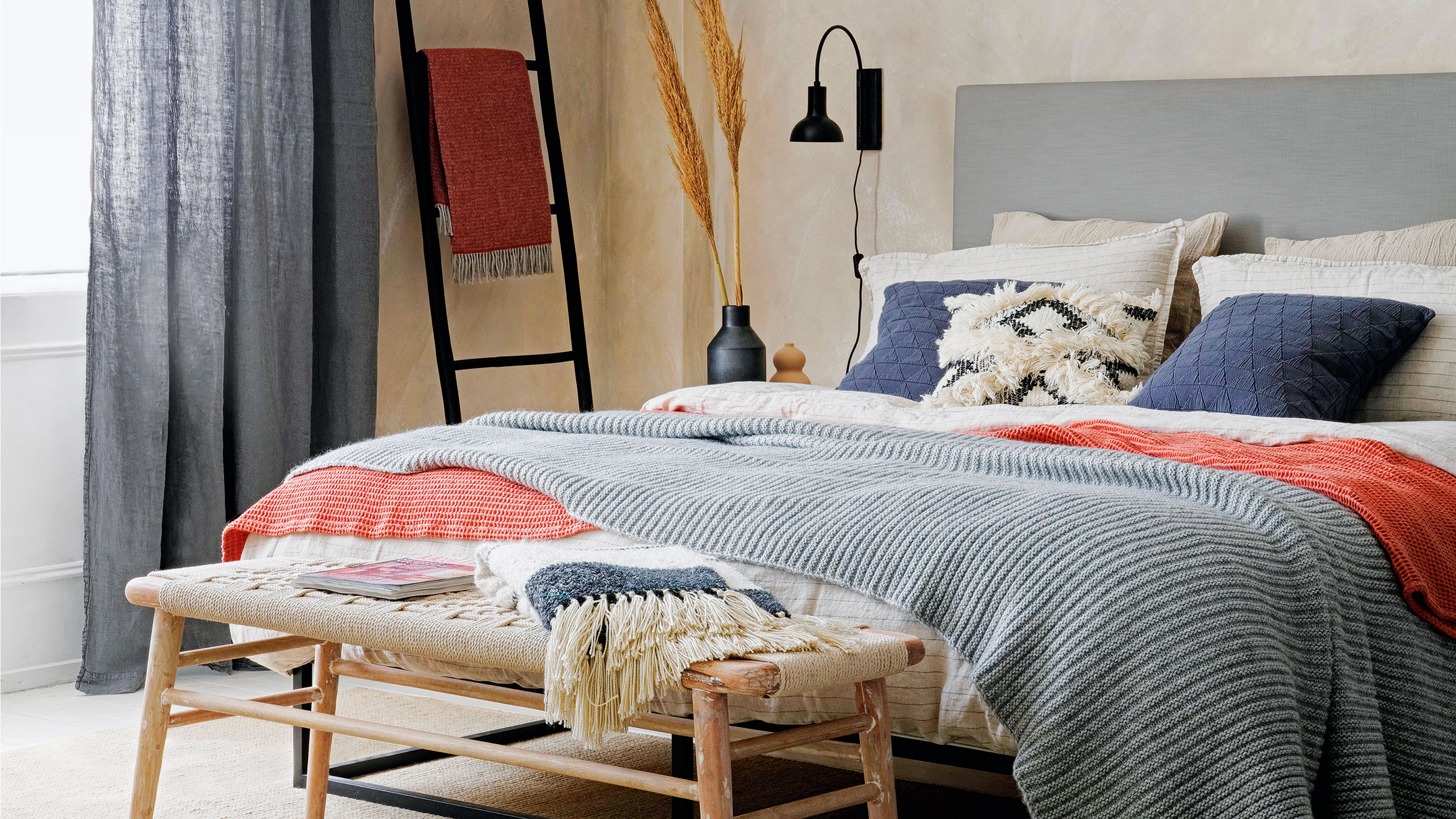 Neutral bedroom with grey upholstered double bed dressed in layered linens including a grey knitted throw