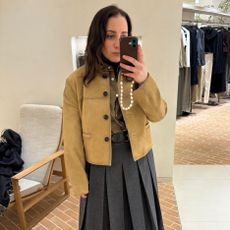 Woman poses in mirror wearing suede jacket and grey skirt.