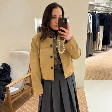 Woman poses in mirror wearing suede jacket and grey skirt.