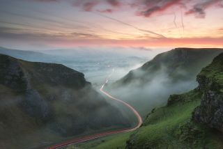 A misty valley with a stream of car brake lights running through it