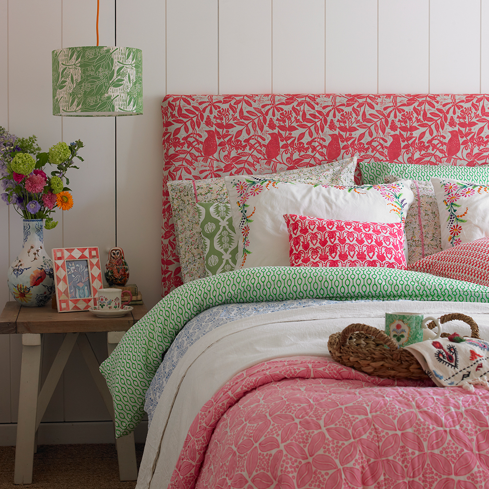 bedroom with white panel wall and red designed bed with coloured cushion