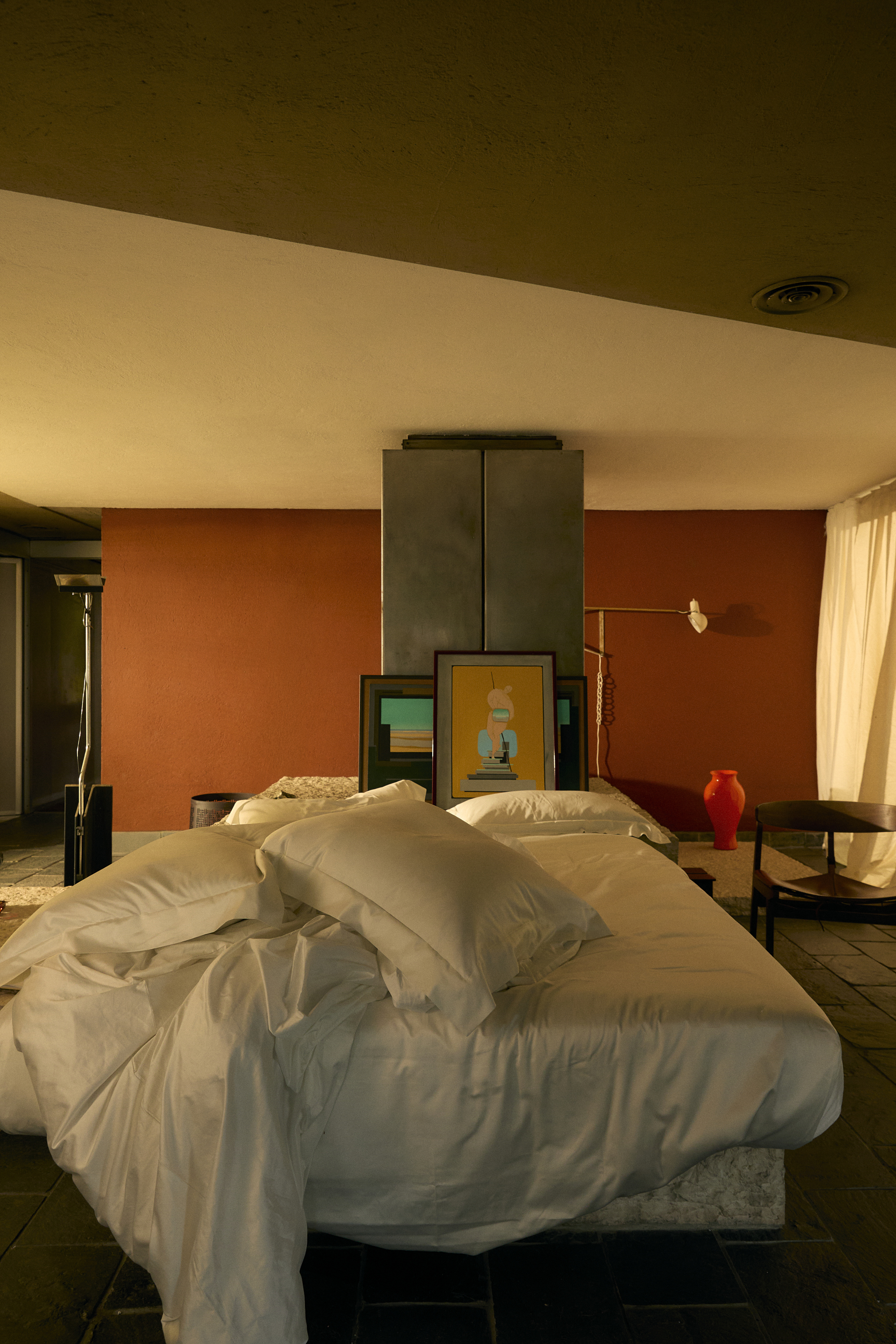 Image of a large bedroom with red walls and a bed in the middle with white satin sheets that is unmade.