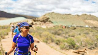 A woman hikes in the desert wearing a hat and sunglasses