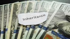 A ripped piece of paper with the word "inheritance" rests on top of a few $100 bills.