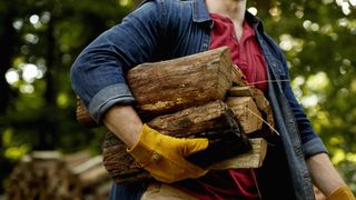 Man carrying firewood in one arm wearing a yellow rubber glove.