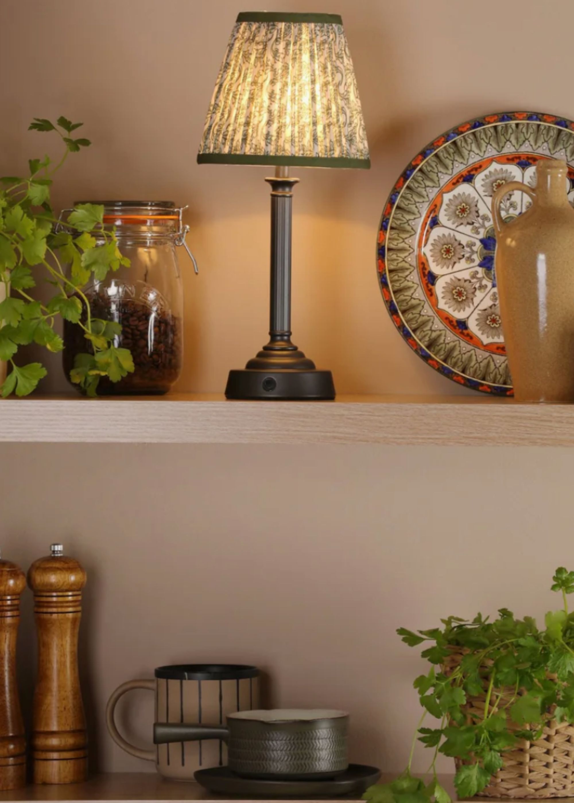 A portable lamp on a kitchen shelving unit with kitchen dishes, herbs and jars around it