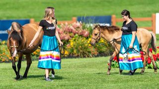 two ladies in costume with two ojibwe ponies