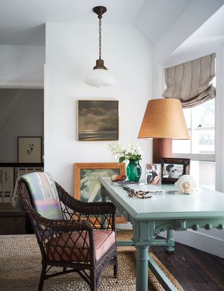 green writing table and wicker chair in window with sisal mat and paintings