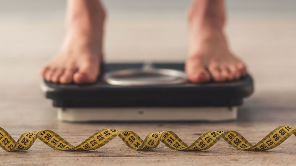 Feet on bathroom scales and tape measure on floor