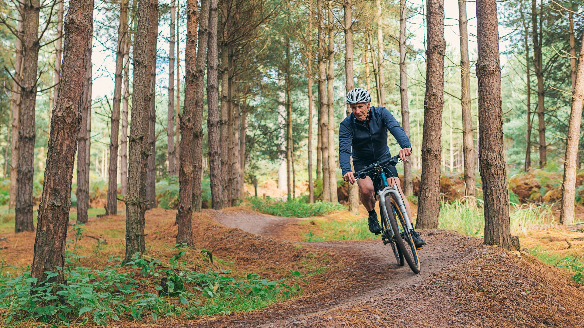 Senior man cycling through forest