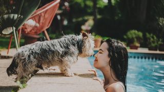 women in pool kissing her dog standing on the pool side