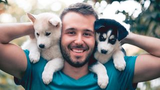Cheerful young man holding two Husky puppies