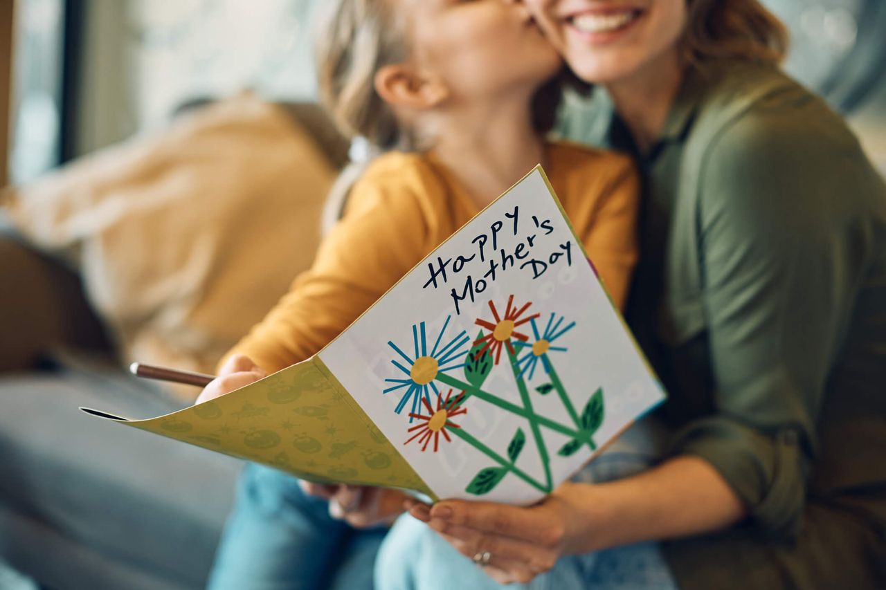 A happy mother and her daughter cuddling while holding a homemade mother&#039;s day card.