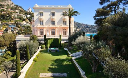 A three floor mansion with a long front garden, nestled away in the hillside with the beach in the background. 
