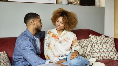 A young couple talk seriously while sitting on their sofa.